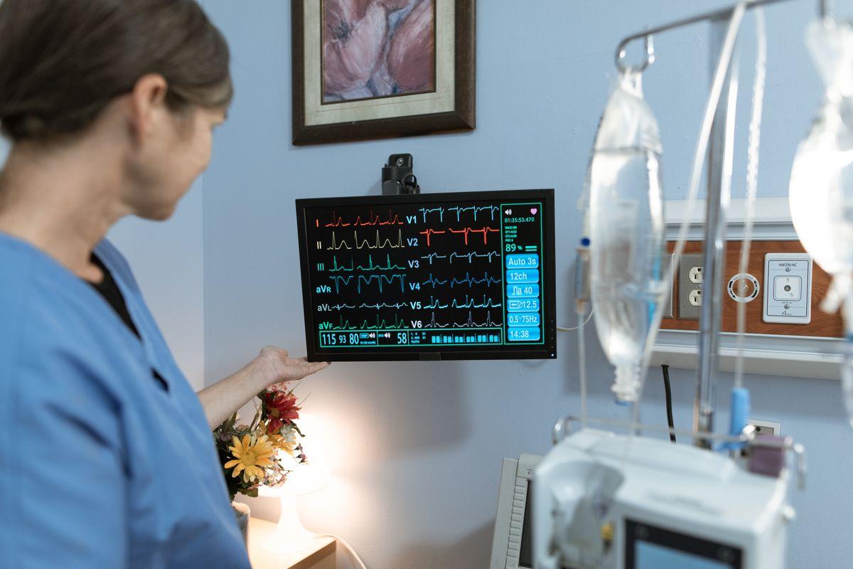 Enfermeira apontando para traçado de eletrocardiograma em monitor de beira-leito hospitalar