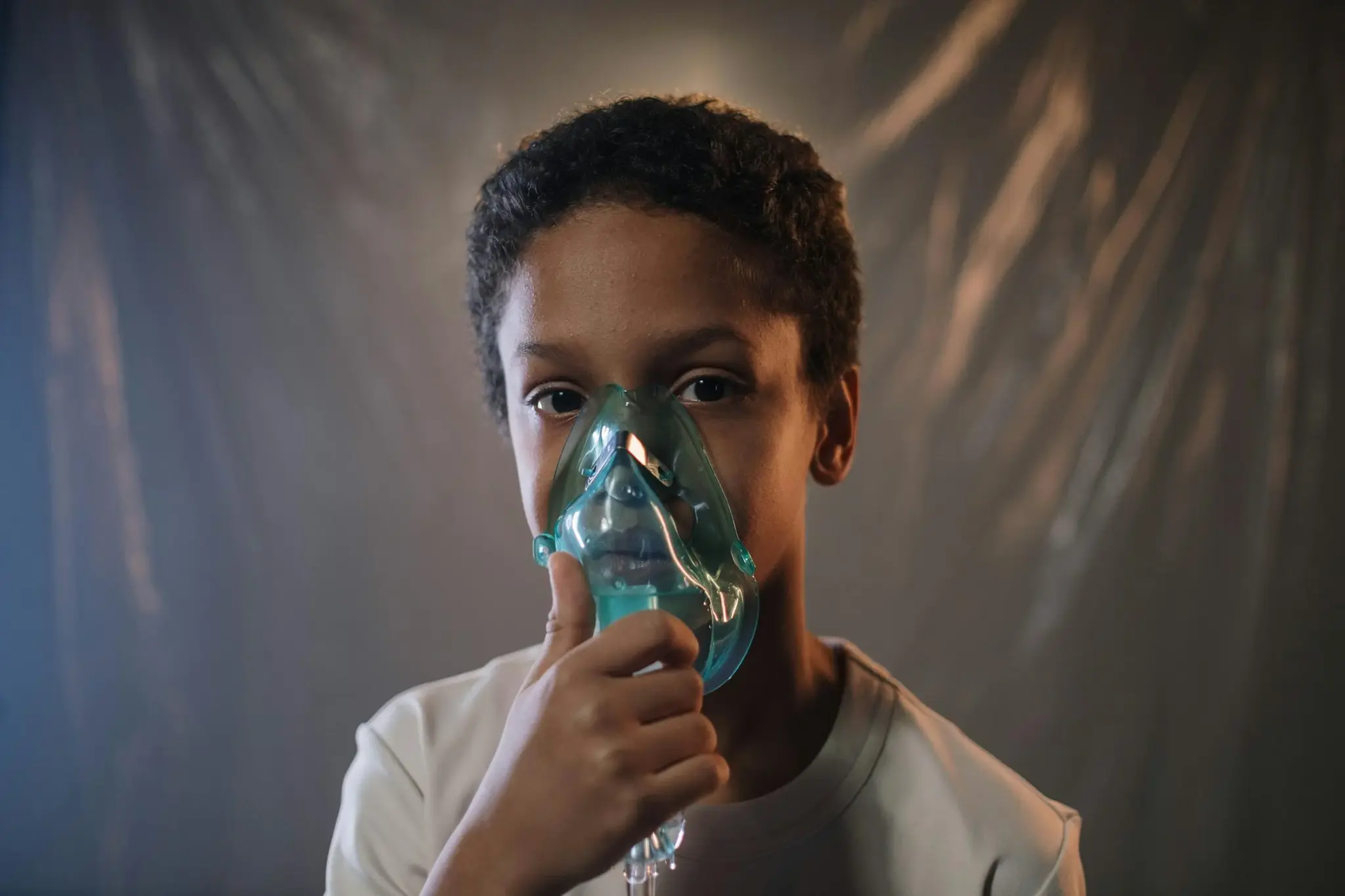 Menino usando máscara de nebulização transparente sobre nariz e boca durante tratamento respiratório