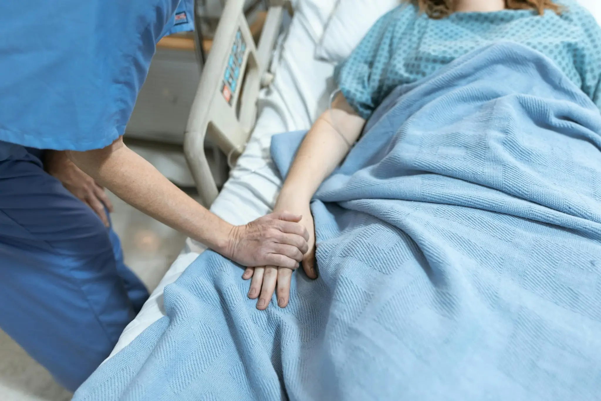 Profissional de saúde segurando a mão de paciente internado em leito hospitalar como gesto de acolhimento