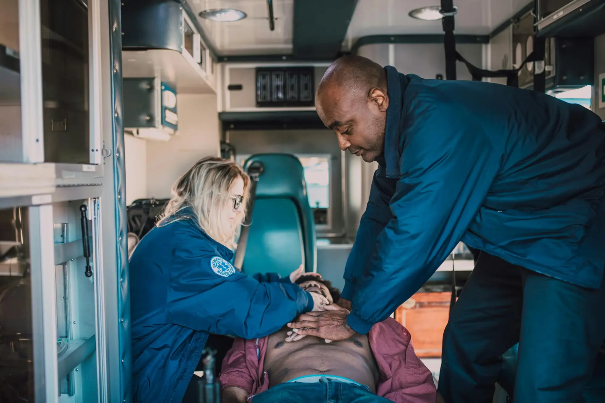 Dois socorristas realizando compressões torácicas em paciente dentro de ambulância