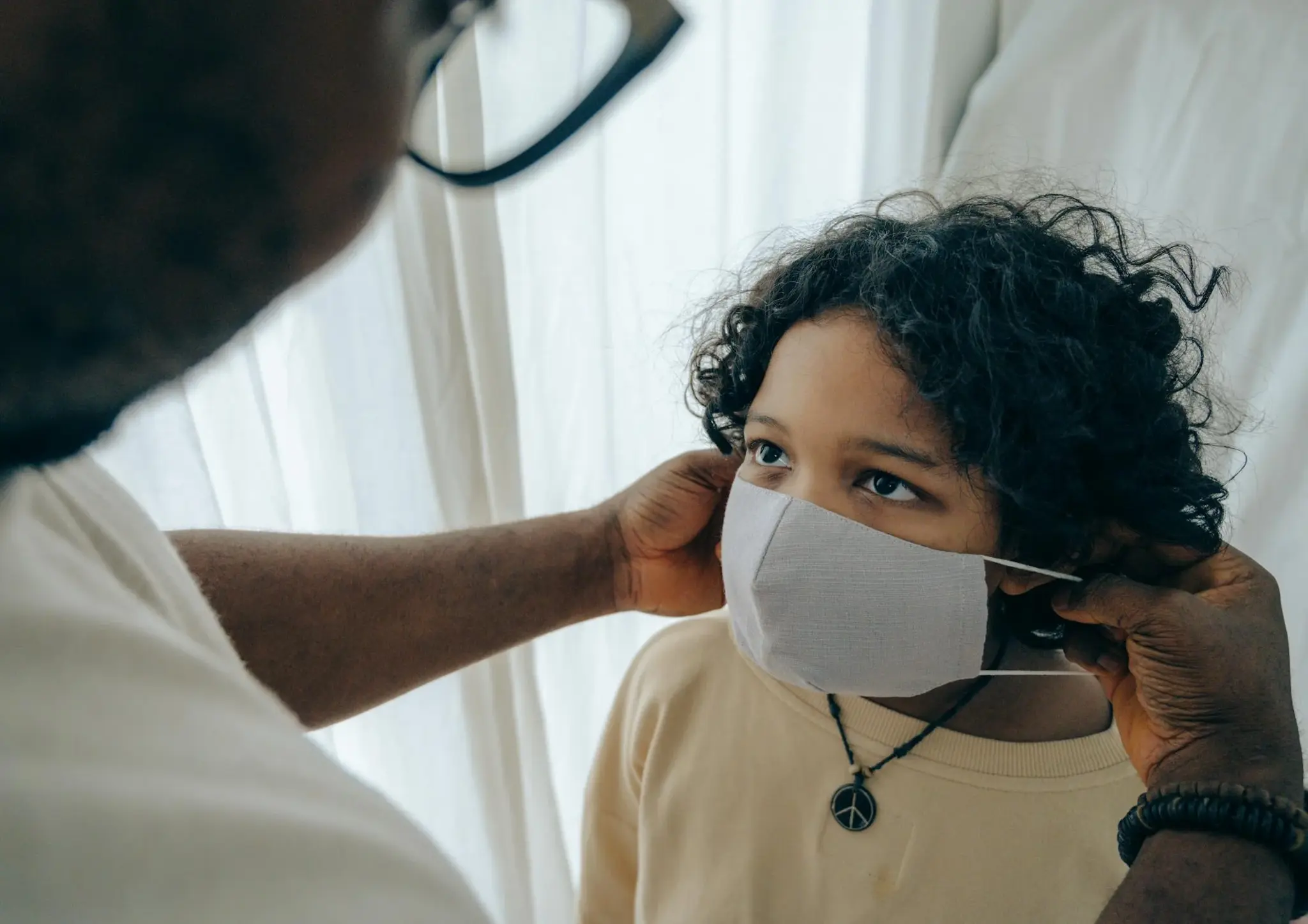 Adulto ajustando máscara de proteção facial de pano no rosto de uma criança
