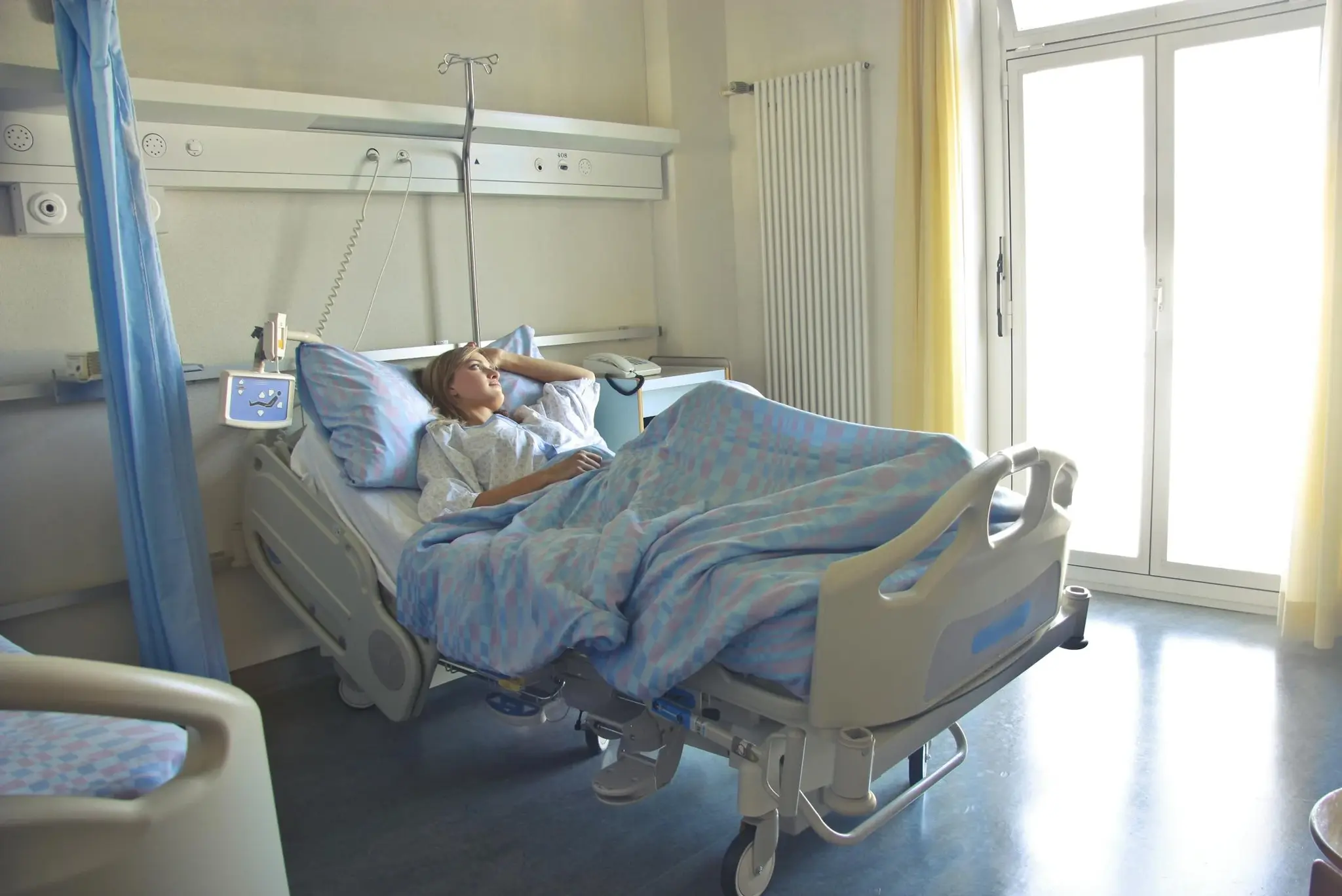 Paciente internada em leito hospitalar olhando pela janela, com suporte de soro ao lado da cama