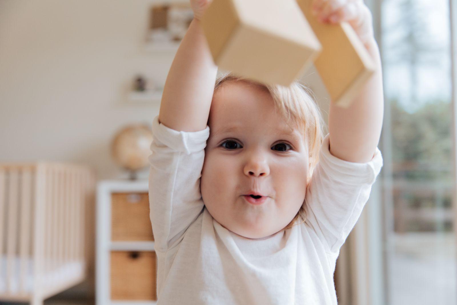Bebê pequeno com os braços levantados segurando um brinquedo, ilustrando o risco de objetos pequenos ao alcance de lactentes