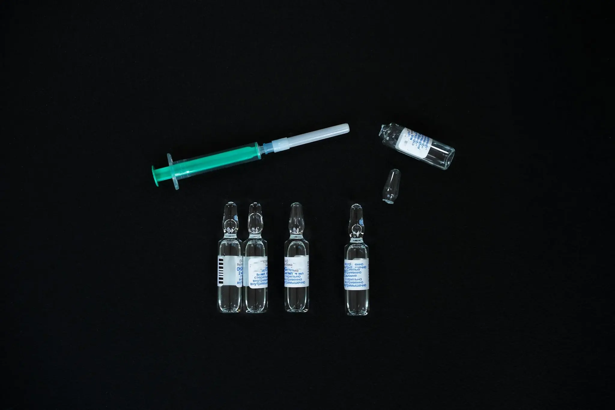 Ampolas de medicação injetável e seringa preenchida dispostas sobre fundo preto