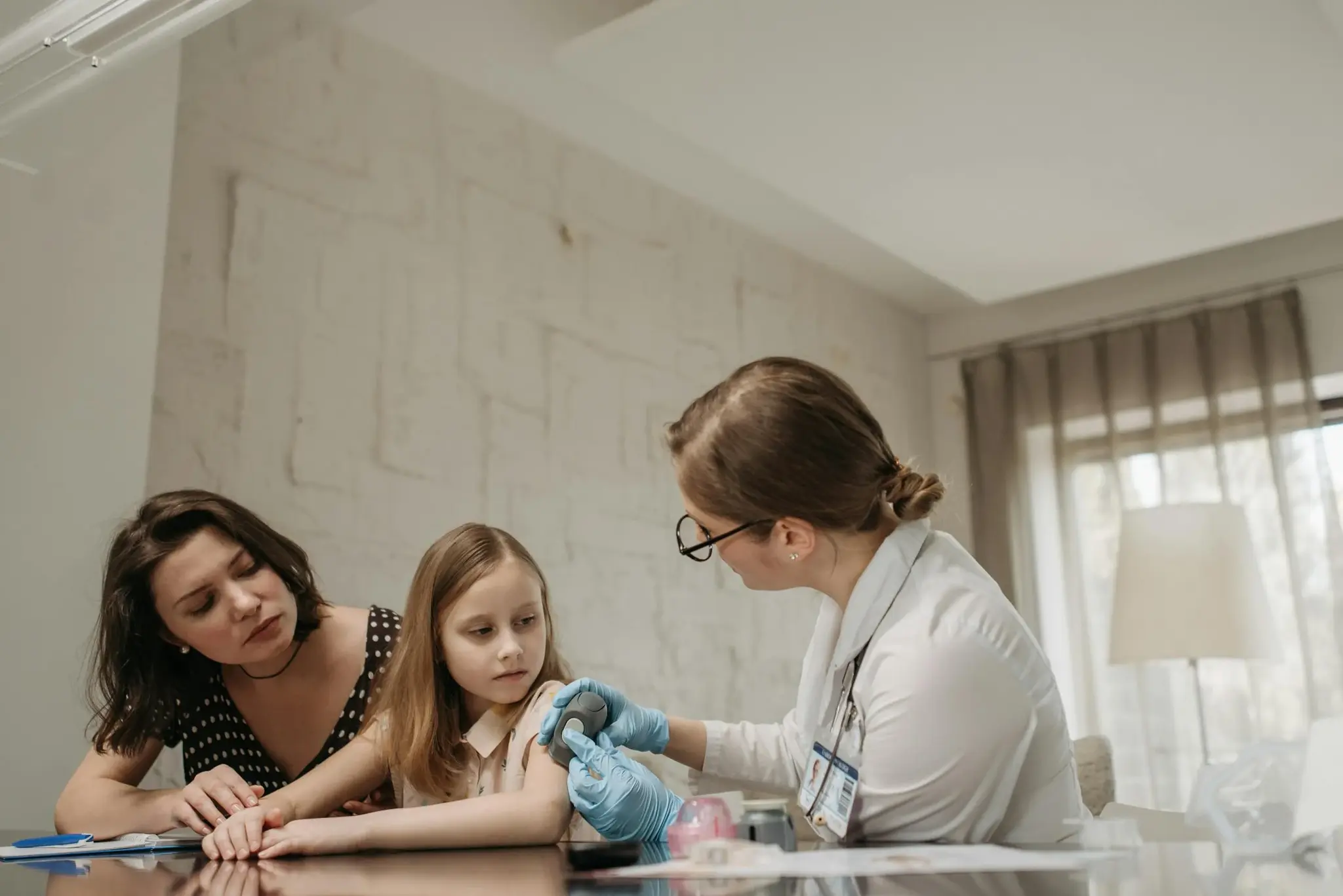 Médica aplicando dispositivo de monitorização no braço de uma criança durante consulta, com a mãe acompanhando