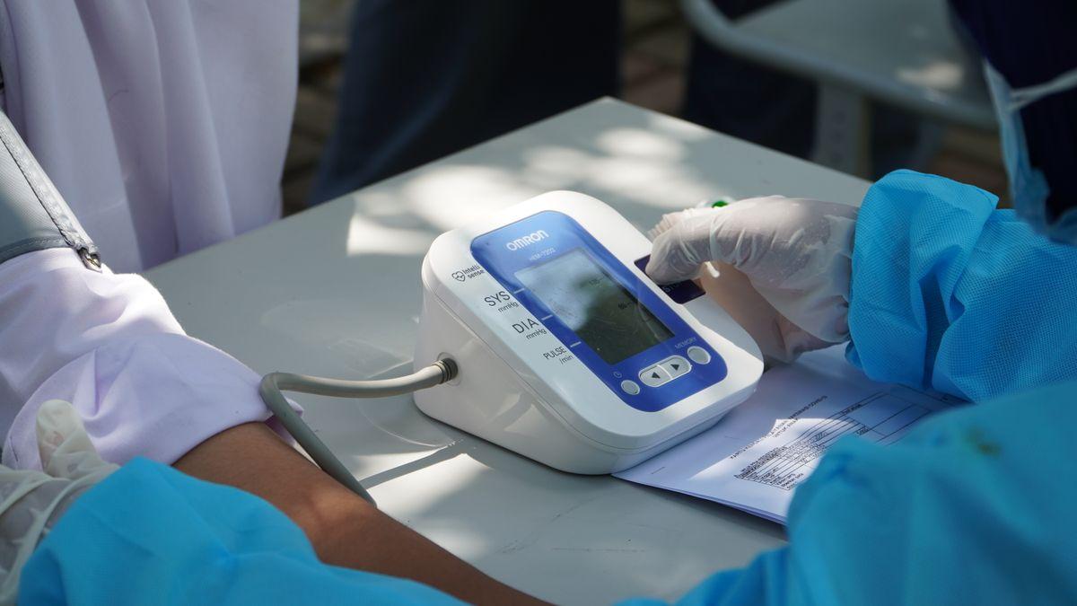 Profissional de saúde com luvas medindo a pressão arterial de um paciente com aparelho digital Omron